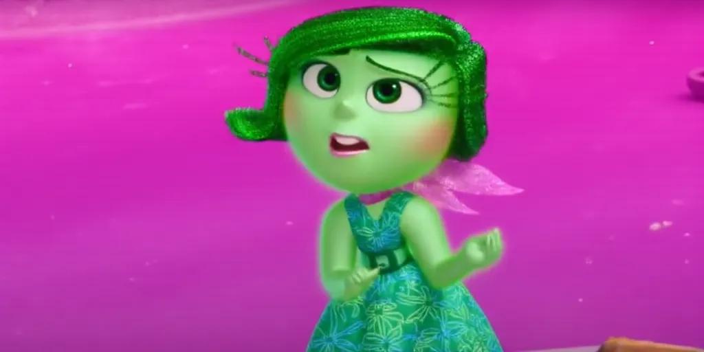 A character from the animated movie "Inside Out" named Disgust. She is depicted with bright green skin and short, green hair. She is wearing a green dress with an intricate swirl design and has a pink scarf around her neck. The background features pink and purple tones.